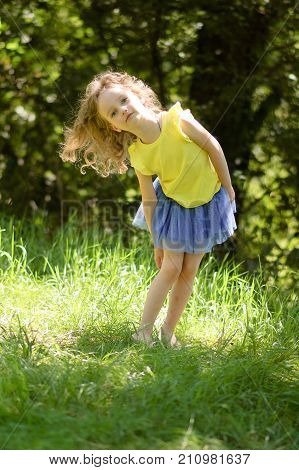 Outdoors Portrait of Cute Blond Girl in Bright Clothing Posing in the Park During Sunny Day and Looking at the Camera