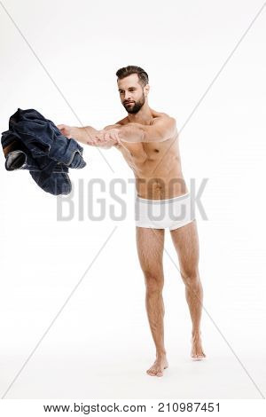 He does not need them anymore! Full length of handsome shirtless young man throwing away his jeans and looking away while standing against white background.