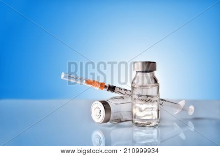 Vials And Syringe On White Table With Blue Background
