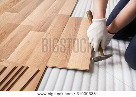 Installing Laminated Floor, Detail On Man Hands Fixing One Tile With Hammer, Over White Foam Base La