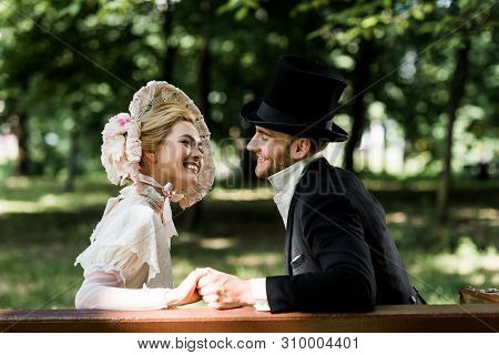 Handsome Aristocratic Man Holding Hands With Cheerful Victorian Woman In Hat