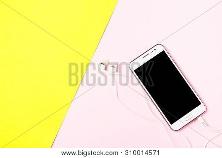 Smartphone With Earphones On Art Yellow And Pink Background. Top View
