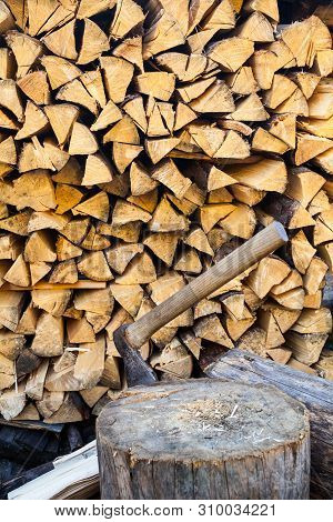 Axe In A Stump Near The Stack Of Chopped Firewood Logs. Wood Splitting. Close-up.