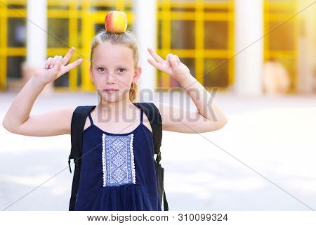 Happy Girl With Apple On Her Head. Great Portrait Of School Pupil Outside Classroom Carrying Bag. Ba