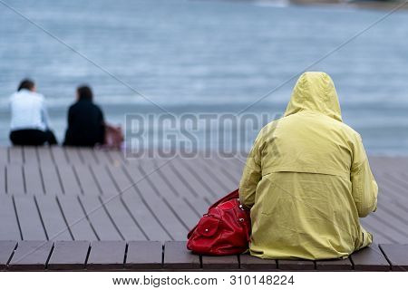 A Woman In A Yellow Raincoat Sits On The Beach