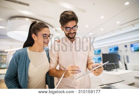 Attractive Young Hipster Couple Checking Out A Tablet With An Electric Pen While Shopping In The Ele