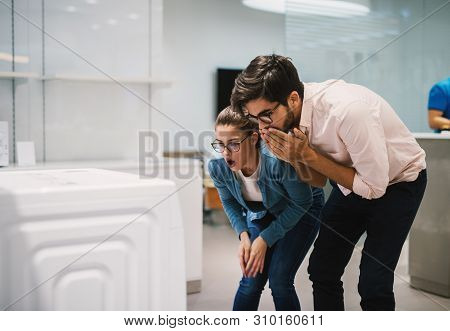 Surprised Young Modern Couple Looking At Laundry Machine In The Electronic Shop.