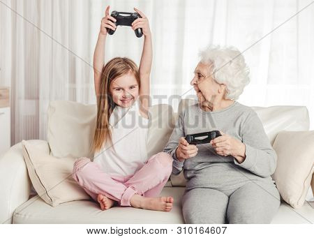 Smiling grandmother with little granddaughter playing games together with gamepads