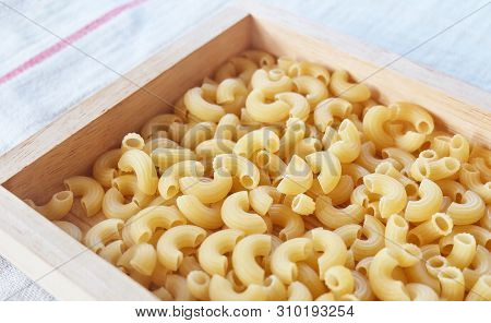 Food And Cuisine, Uncooked And Dried Elbow Macaroni Or Gomiti Pasta In A Wooden Tray.