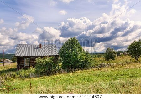 Russian Village In Summer. View Of The Traditional Log House With A Rickety Wooden Fence. Village Of