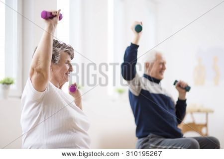 Elderly Man And Woman Exercising With Dumbbells During Physiotherapy Session At Hospital