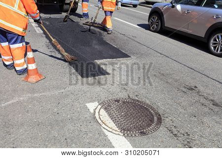 The Working Team Smoothes Hot Asphalt With Shovels, Level And Broom By Hand When Repairing The Road.