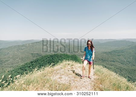 Sporty Hiker Girl In A T-shirt And Shorts Is Walking With Trekking Poles Along The Ridge Of A Mounta