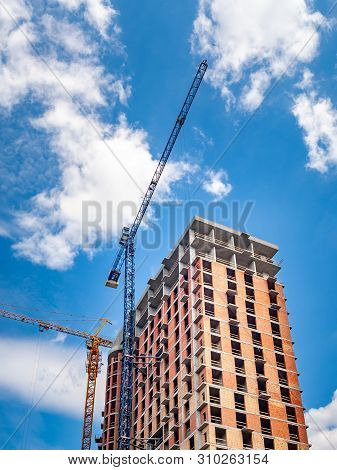 Construction Site With Cranes Against A Blue Sky With White Clouds. Bottom View Of The Construction 