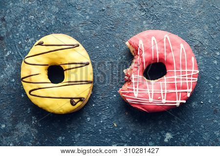 Pink Frosted Donut With Bite Missing And Yellow Donut On Dark Background. Top View.