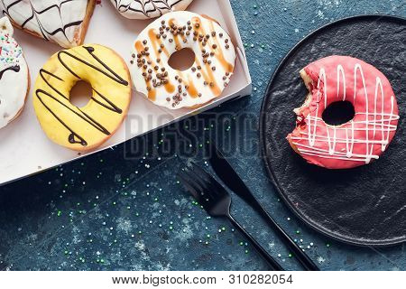 Pink Frosted Donut With Bite Missing On A Plate With Assortment Donuts Box On Dark Background. Top V