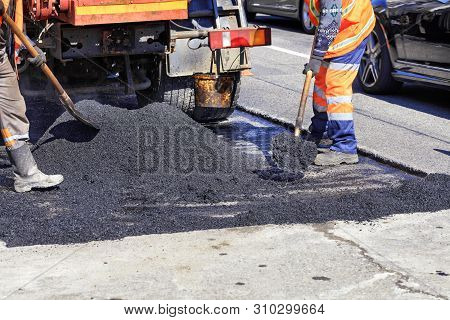 The Working Crew Evenly Distributes Hot Asphalt With Shovels Manually On The Repaired Site Of The Ro