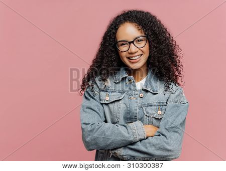 Horizontal Shot Of Mirthful Pleasant Looking Female Model Wears Optical Glasses And Jean Jacket, Kee