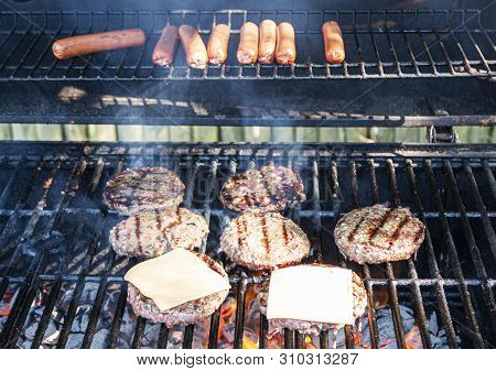 Hot Dogs, Hamburgers And Cheesburgers Are Cooking On A Grill With Hot Coals Underneath.