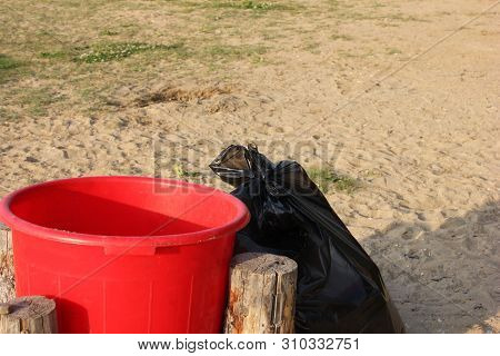 Red Plastic Garbage Collection Tank And Black Plastic Garbage Bag Full Of Garbage Nearby. Garbage Co