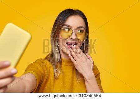 Stylish Young Woman In Bright Sunglasses Covering Mouth With Hand And Looking Away While Taking Self