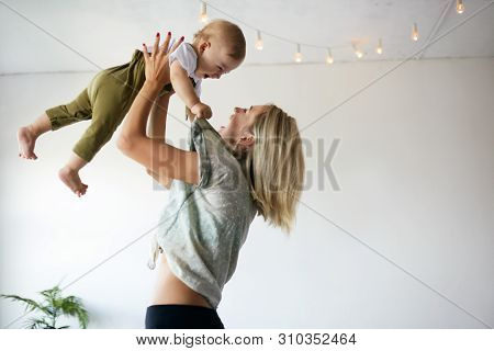 Indoor Image Of Casually Dressed Blond Woman On Maternity Leave Tossing Her Cute Barefooted Laughing