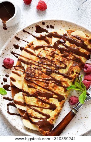 Crepe With Chocolate Paste, Banana And Raspberries On A Concrete Background. Tasty Breakfast.