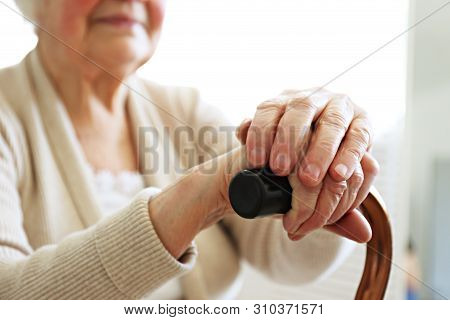Elderly Woman Sitting In Nursing Home Room Holding Walking Quad Cane With Wrinked Hand. Old Age Seni
