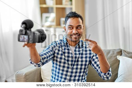 blogging, videoblog and people concept - smiling indian male video blogger with camera videoblogging at home