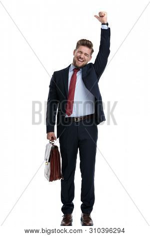 Happy businessman celebrating and holding his briefcase while wearing an elegant blue suti and standing on white studio background