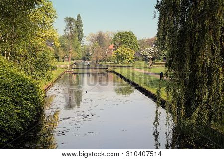 A Couple Crossing A Wooden Bridge Over A Canal At A Park In Bussum, The Netherlands. The Beautiful S
