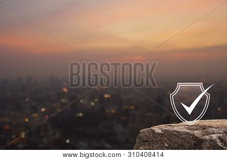 Security Shield With Check Mark Flat Icon On Rock Mountain Over Blur Of Cityscape On Warm Light Sund