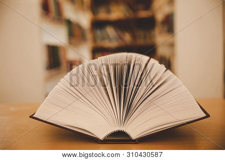 Opened Book On The Desk And Isle Of Bookshelves In School Study Class Room Background For Academic E