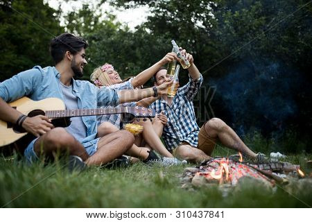 Group Of Friends Camping.they Are Sitting Around Camp Fire, Playing Guitar