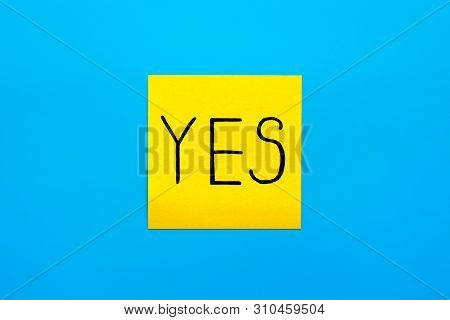 Close Up Black Handwritten Inscription Yes Word On One Yellow Square Sticker On Blue Background With