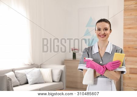 Portrait Of Young Chambermaid With Cleaning Supplies In Hotel Room. Space For Text
