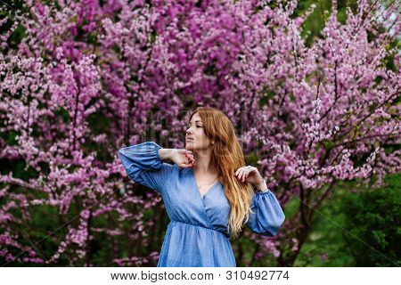 Beautiful Smilling Redhead Woman In Spring Time Blossom Cherrytrees Garden. Perfect Time For A Walk.