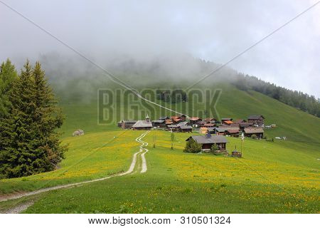Green Meadow And Village Obermutten On A Foggy Summer Day.