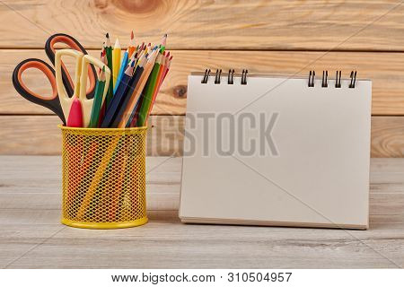 Pencils In Metal Basket And Blank Notebook. Set Of Colored Pencils With Scissors In Metal Holder And