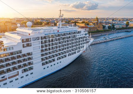 Cruise Liner Moored At The Embankment In The Waters Of The River In The Evening At Sunset. Aerial To