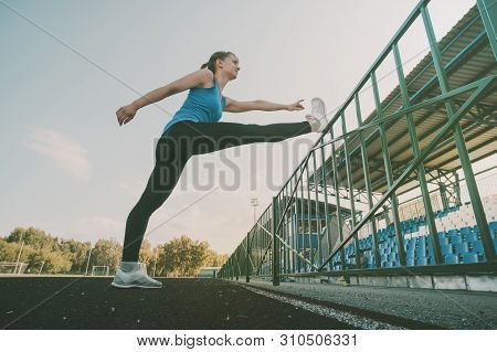 Young Slim Blond Woman At Green Grass Of Stadium In The Morning Making Exercises. Healthy Lifestyle 