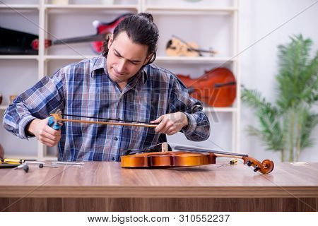 Young handsome repairman repairing violin