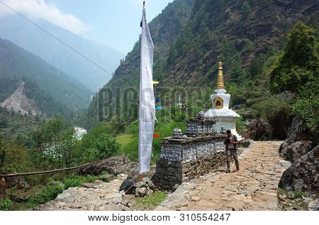 Khumbu valley, Solukhumbu, Nepal - May 9, 2019: Nepali man walking next to buddhist stupa, mani wall and praying flag. The trail is the part of Everest bace camp trek, near Chaurikharka
