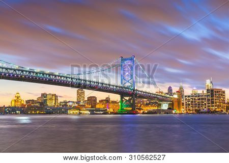 Philadelphia, Pennsylvania, USA skyline on the Delaware river with Ben Franklin Bridge at night.