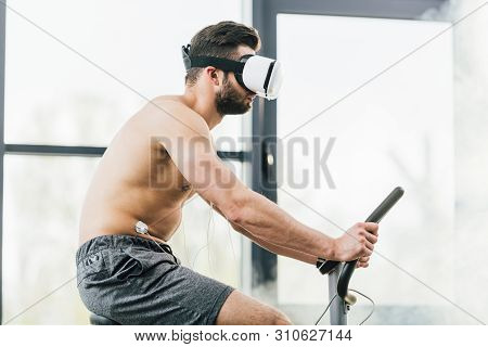 Shirtless Sportsman In Virtual Reality Headset With Electrodes Training On Elliptical During Enduran