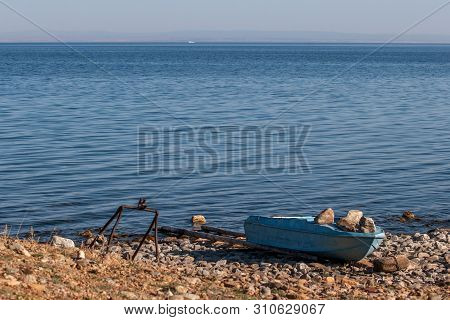 Fishing Boat On The Shore Of The Blue Lake Baikal. Pressed Down By Large Stones. Near The Iron Devic