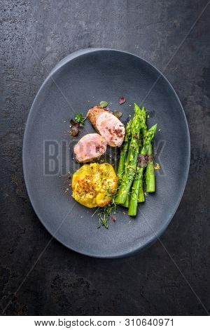 Fried Iberian pork fillet sliced with blanched green asparagus and potato gratin dauphinois with spice as top view on a cast iron design plate 