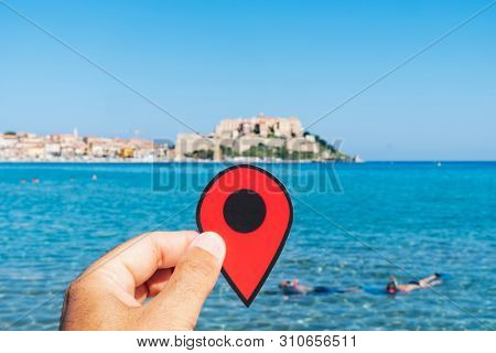 closeup of the hand of a young caucasian man with a red marker pointing the Mediterranean sea in Calvi, Corsica, France, with the Calvi citadel in the background
