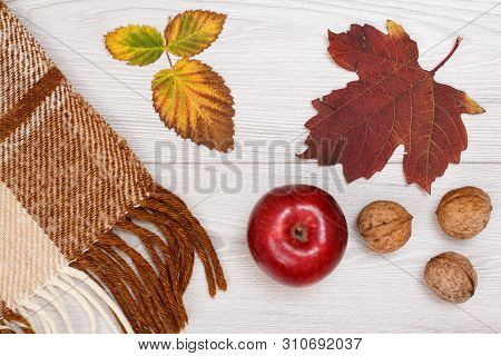Checkered Plaid, Dry Yellow And Brown Leaves, Red Apple And Walnuts On Wooden Background. An Autumn 