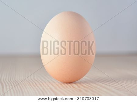 Egg Standing On Its Fat End On Wooden Surface.
